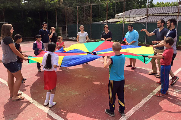 Children playing a game with a colorful parachute and a ball.