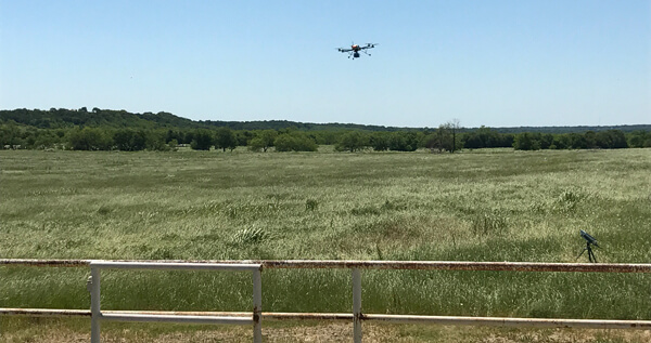 Drone flying over farm land with a metal fence in the foreground.