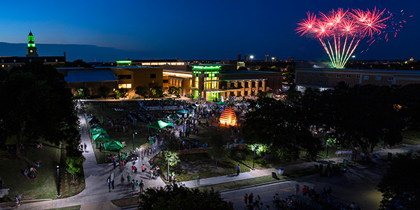 Overhead night photo of the UNT 2018 Block Party with fireworks in the distance