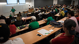 Students seating in a large classroom listen to a professor